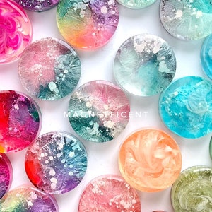 May include: Assortment of colourful round resin coasters with abstract swirling patterns and glitter. The coasters are approximately 2 inches in diameter. The text "MAGNIFICENT" is visible in the image.