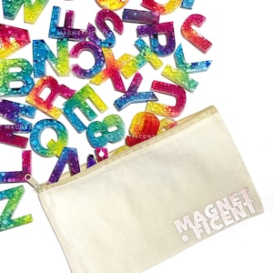 May include: A set of colorful alphabet magnets with a rainbow tie-dye design and glitter embedded in the resin. The magnets are in a white canvas zippered pouch with the text "MAGNETFICENT" printed on the front.