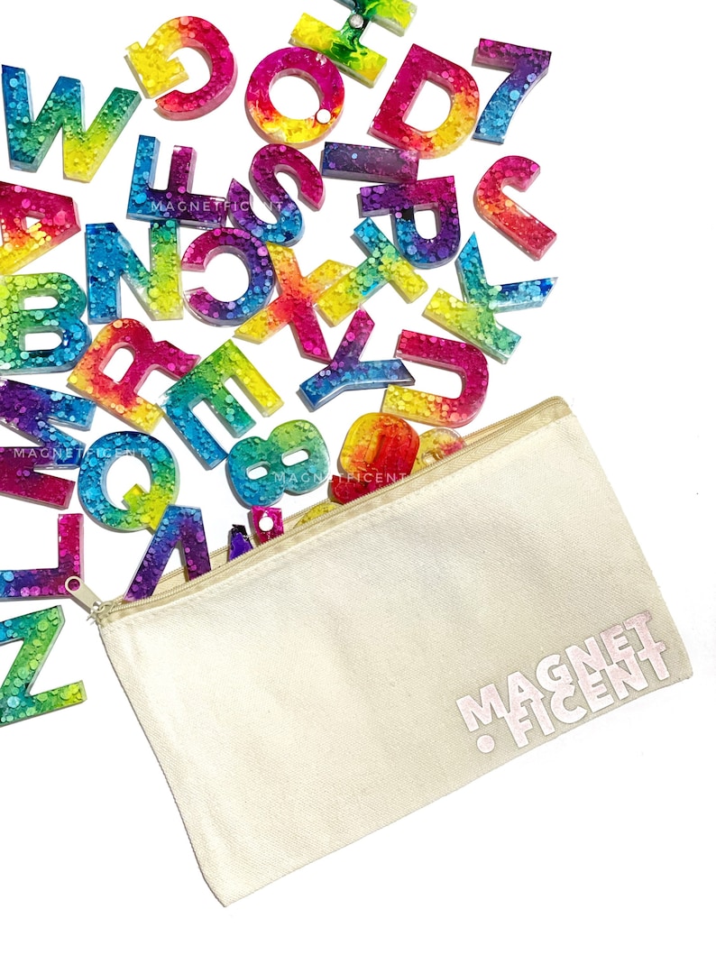 May include: A set of colorful alphabet magnets with a rainbow tie-dye design and glitter embedded in the resin. The magnets are in a white canvas zippered pouch with the text "MAGNETFICENT" printed on the front.