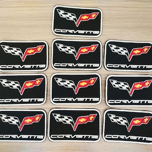 Op de afbeelding: Tien zwarte en witte geborduurde patches met het woord "Corvette" en een gestileerd rood-wit geruit vlagontwerp.