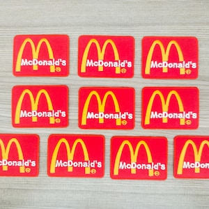 Könnte beinhalten: Zehn rote Stoff-Patches mit dem McDonald's-Logo der goldenen Bögen und dem Text "McDonald's" in Weiß.