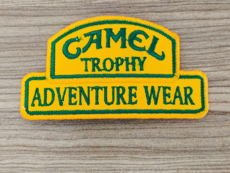 May include: Yellow and green embroidered patch with the text "Camel Trophy Adventure Wear".