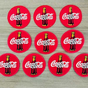 Puede incluir: Diez parches redondos de Coca-Cola rojos con un contorno blanco. Cada parche presenta un logotipo de Coca-Cola blanco y una botella de Coca-Cola.