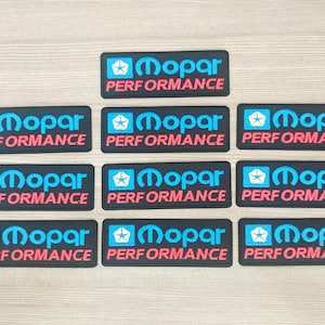 Puede incluir: Diez parches bordados en blanco y negro con el logotipo de Mopar en azul y blanco y el texto "Mopar Performance" en rojo.