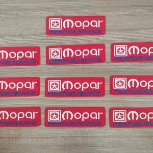Puede incluir: Diez parches rectangulares rojos con texto blanco que dice "Mopar Performance" y una estrella azul y un logotipo M estilizado.