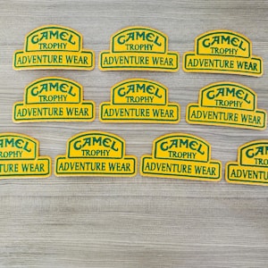 May include: Ten yellow and green stickers with the text "Camel Trophy Adventure Wear" repeated on each sticker.