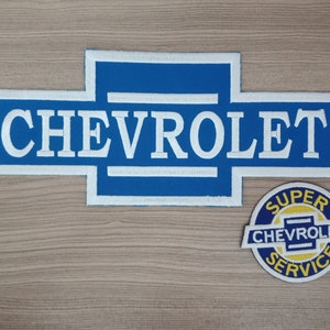 May include: Two blue and white embroidered patches with the word "CHEVROLET" in white. The larger patch is a classic Chevrolet logo. The smaller patch is a circle with the words "SUPER CHEVROLET SERVICE" in yellow.