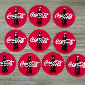 Pode incluir: Nove patches redondos vermelhos para passar a ferro com o logotipo da Coca-Cola e uma garrafa de Coca-Cola em branco.