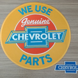 Puede incluir: Un parche redondo amarillo con el texto "WE USE Genuine CHEVROLET PARTS" en letras azules y blancas. El logotipo de Chevrolet está en el centro del parche. Un parche azul más pequeño con el logotipo de Chevrolet está debajo del parche más grande.