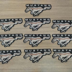 May include: Ten black and white iron-on patches featuring the word "Mustang" and a stylised horse design.