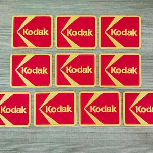 Peut inclure: Dix patchs carrés rouges et dorés avec le mot "Kodak" imprimé en lettres blanches.