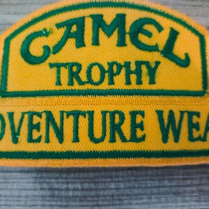 May include: A yellow and green embroidered patch with the text "Camel Trophy Adventure Wear".