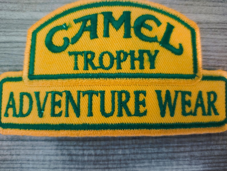 May include: A yellow and green embroidered patch with the text "Camel Trophy Adventure Wear".