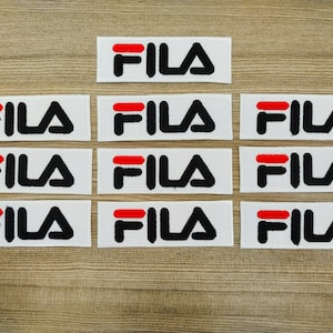 May include: Ten white fabric patches with the word "FILA" printed in black letters with a red stripe above the word.