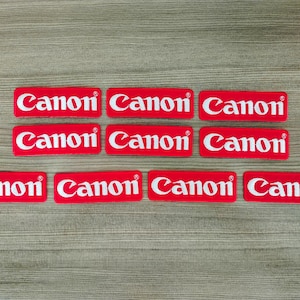 Op de afbeelding: Acht rode rechthoekige plekken met het woord "Canon" in witte letters.