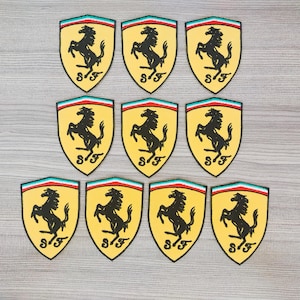 May include: Ten yellow and black iron-on patches featuring the Ferrari logo, a black horse rearing up on its hind legs, with the letters "S.F." underneath.