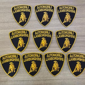 Puede incluir: Diez parches bordados negros y dorados con el texto "Automobili Lamborghini" y un logotipo de toro cargando.