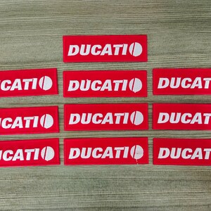 Puede incluir: Diez parches de tela rojos con la palabra "DUCATI" en letras blancas y un círculo blanco.