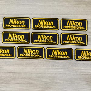 May include: Eight black fabric patches with yellow embroidered text that reads "Nikon Professional".