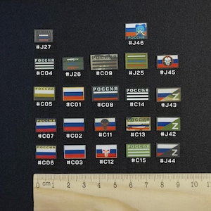 May include: A collection of small, rectangular patches with various designs and the word "Russia" or "Россия" in white. The patches feature flags, cartoon characters, and other symbols. A ruler with centimeter markings is at the bottom.