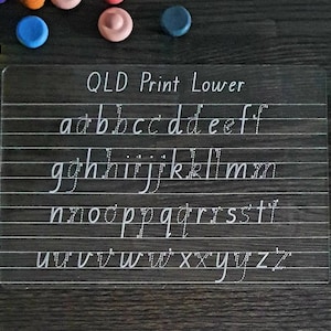 May include: A clear plastic sheet with a white grid and the text "QLD Print Lower" at the top. The lowercase alphabet is written in cursive on the sheet.