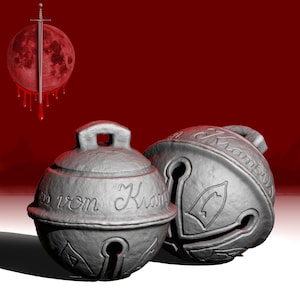 Könnte beinhalten: Zwei silberne Glöckchen mit filigranen Verzierungen und der Aufschrift "aus vom Krampus" auf einem Glöckchen.