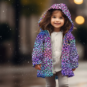Può includere: Un bambino indossa un impermeabile colorato con stampa leopardata. L'impermeabile ha un cappuccio ed è realizzato in materiale impermeabile. Il bambino è in piedi su un marciapiede bagnato.