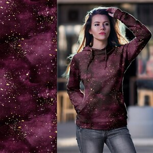 May include: A maroon hoodie with a galaxy print and gold glitter accents. The hoodie has a drawstring hood and a kangaroo pocket.