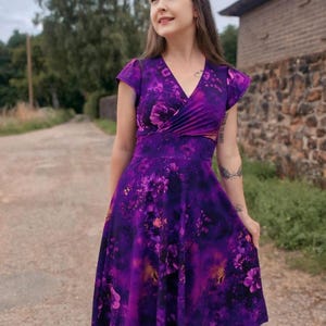 May include: A purple floral print dress with a V-neckline and short sleeves. The dress has a fitted bodice and a flowing skirt.