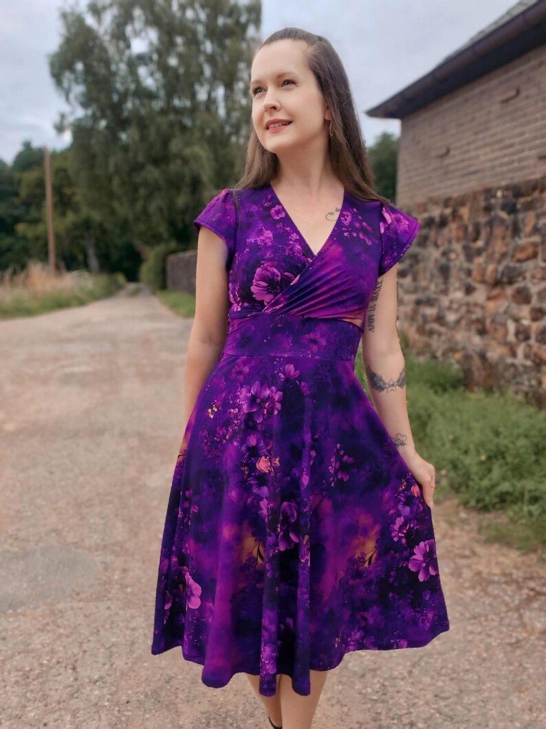 May include: A purple floral print dress with a V-neckline and short sleeves. The dress has a fitted bodice and a flowing skirt.