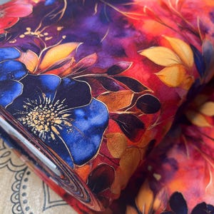 May include: A close-up of a fabric with a watercolor floral print. The fabric features a vibrant red, orange, and purple background with blue flowers and gold accents.