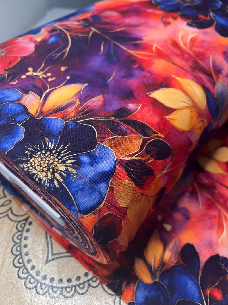 May include: A close-up of a fabric with a watercolor floral print. The fabric features a vibrant red, orange, and purple background with blue flowers and gold accents.