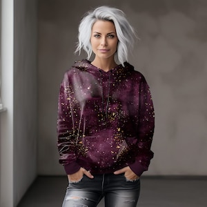 May include: A burgundy hoodie with a galaxy print and gold glitter accents. The hoodie has a drawstring hood and a kangaroo pocket.