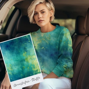 Könnte beinhalten: Eine Frau in einem Auto hält ein Muster aus blauem und grünem Batikstoff. Der Stoff ist mit "Graustufen-Stoffe" beschriftet.