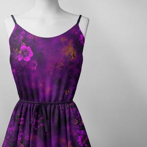 May include: A purple sleeveless dress with a floral print. The dress has a tie at the waist and a flowing skirt.