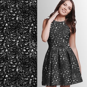 Könnte beinhalten: Ein ärmelloses schwarzes Kleid mit ausgestelltem Rock und hohem Ausschnitt. Das Kleid hat ein sich wiederholendes Leopardenmuster in Grau- und Silbertönen. Der Stoff hat einen subtilen Schimmer, der dem Design einen Hauch von Eleganz verleiht.