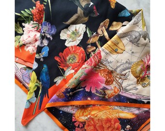 May include: A colorful silk scarf with a floral and celestial design. The scarf features a variety of flowers, birds, and a celestial map. The scarf is trimmed with a bright orange border.