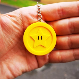 May include: A yellow keychain shaped like a coin with a star in the center. The star has two black eyes.