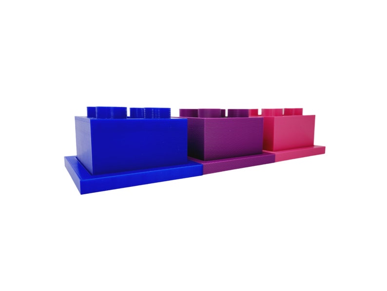 May include: Three stacked plastic building blocks in blue, purple, and pink. The blocks are in the shape of a traditional building block with studs on top.