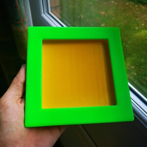May include: A bright green picture frame with a yellow inner border. The frame is made of plastic and has a smooth surface.