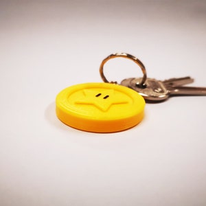 May include: A yellow star-shaped keychain with a black outline and two black dots for eyes. The keychain is attached to a silver key ring and two keys.