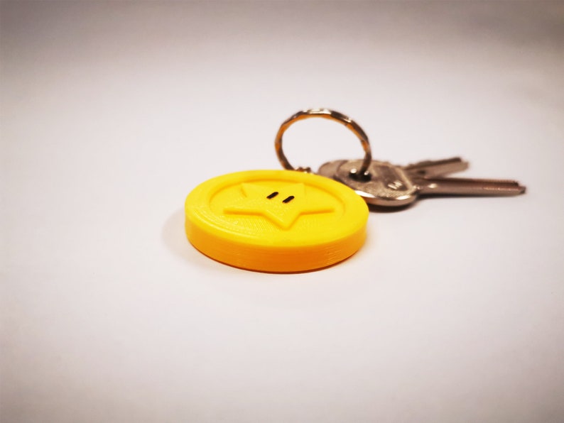 May include: A yellow star-shaped keychain with a black outline and two black dots for eyes. The keychain is attached to a silver key ring and two keys.