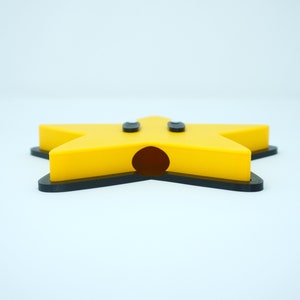 May include: A yellow star-shaped object with two black eyes and a large black mouth. The star is made of plastic and has a black outline.