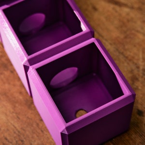 May include: A set of three purple 3D printed boxes with circular openings. The boxes are stacked on top of each other.