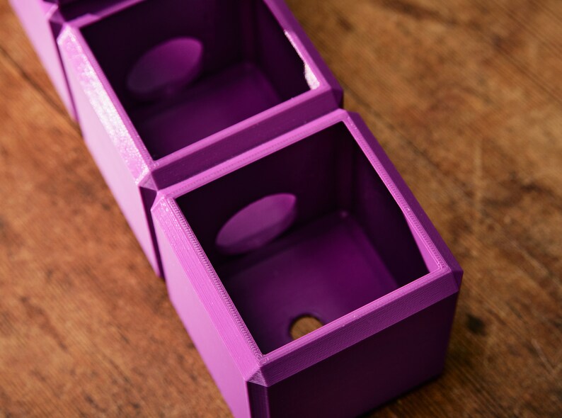 May include: A set of three purple 3D printed boxes with circular openings. The boxes are stacked on top of each other.