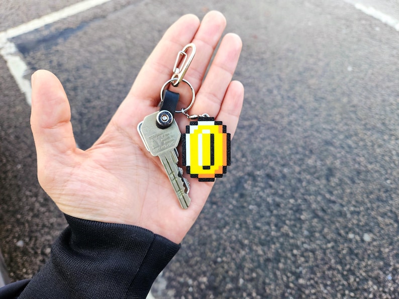 May include: A silver key with a black and silver keychain attached to a gold pixelated coin charm.
