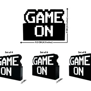 May include: A set of three black and white pixelated "GAME ON" signs. The signs are made of small blocks and come in three sizes: 4, 6, and 8 blocks. The signs are 4.5 inches wide and 3.5 inches tall.