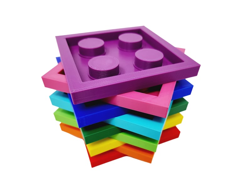 May include: A stack of colorful plastic toy building blocks in the shape of a square with rounded corners. The top block is purple and has four indented circles. The other blocks are pink, blue, green, yellow, and red.