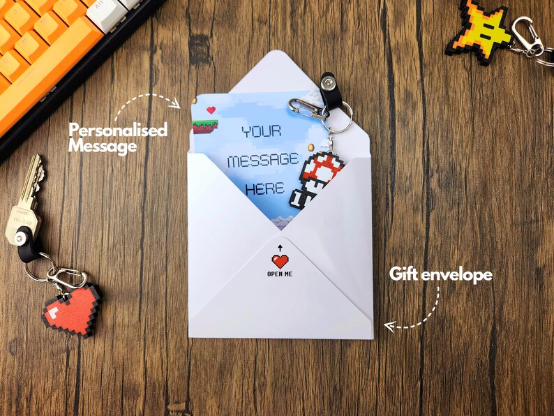 May include: A white envelope with a pixelated video game character on the front. The envelope has a red heart with the words "Open Me" printed on it. The envelope is on a wooden surface.