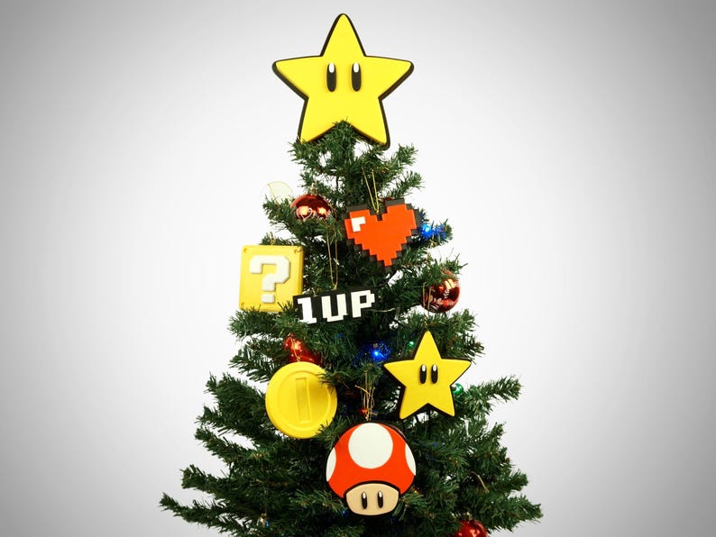 Puede incluir: Un &aacute;rbol de Navidad verde decorado con adornos que representan personajes y objetos de la franquicia de videojuegos Super Mario, incluyendo una estrella amarilla, un coraz&oacute;n rojo, un bloque de signo de interrogaci&oacute;n, un hongo 1-up, una moneda de oro y un hongo rojo.